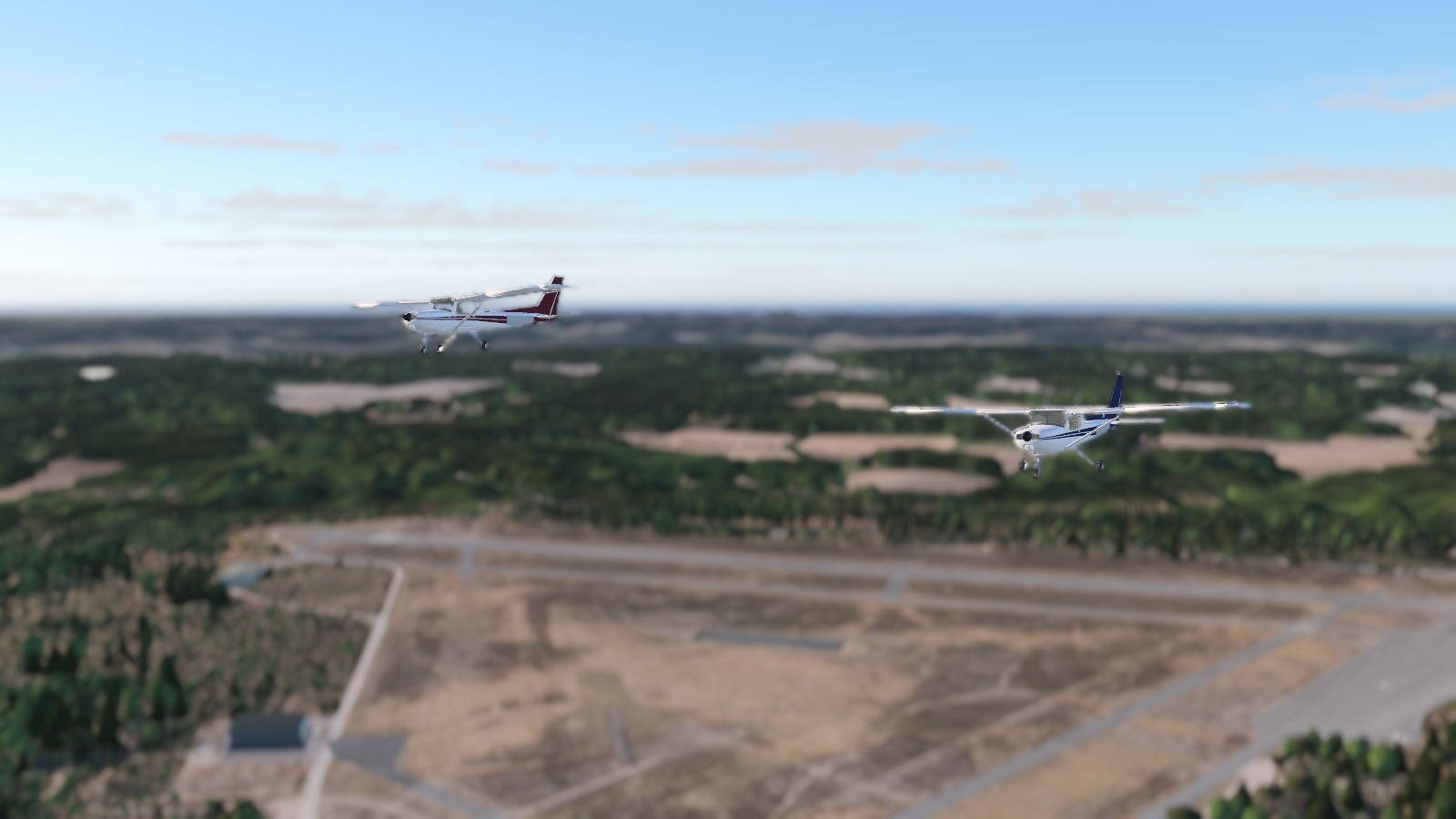 A blue and a red Cessna 152 flying close together, with the Vesivehmaa landscape softly out of focus behind them